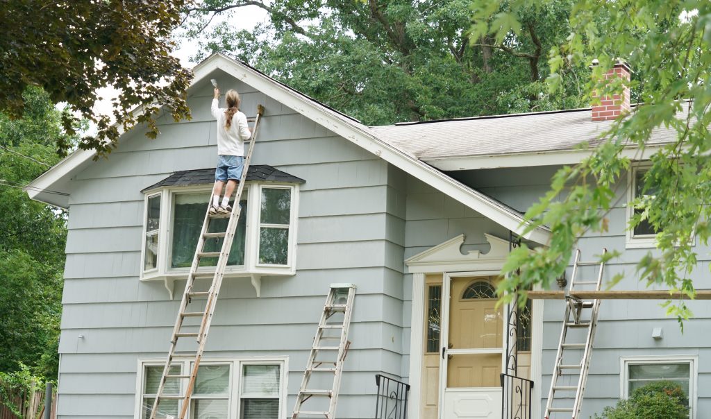 person working on ladder against a blue house