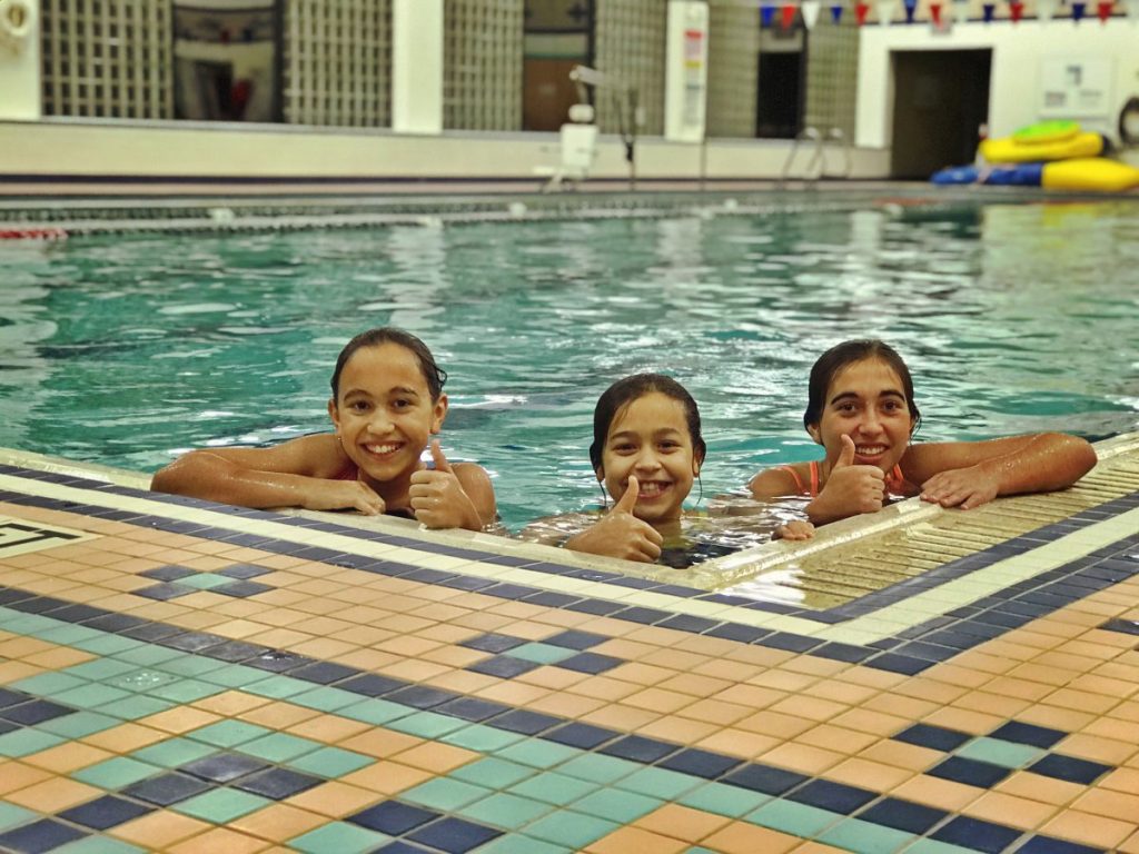 Courtesy of the Greater Wilkes-Barre Family YMCA. 3 Girls smile with thumbs up while in the pool at Greater Wilkes-Barre Family YMCA.