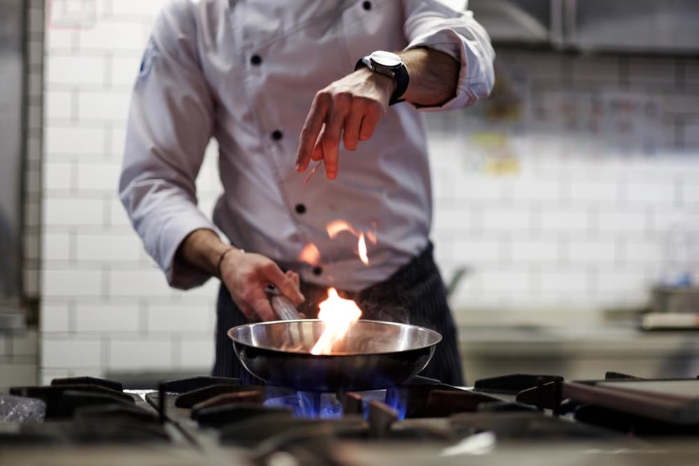 A man cooking in a kitchen with gas flame showing.