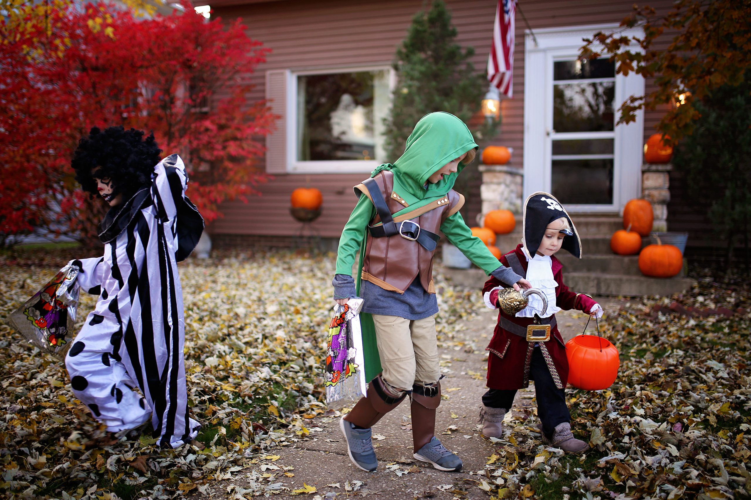 Three cute young kids dressed in costumes are Trick or Treating on Halloween in a small American town.