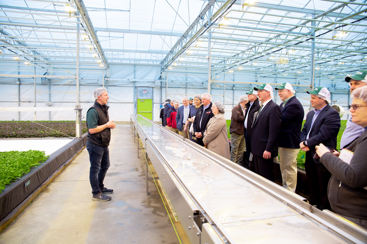 Man speaks to group of people in a greenhouse.