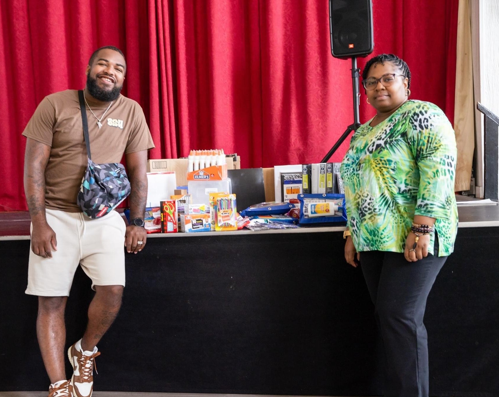 Two people stand next to donated school supplies.
