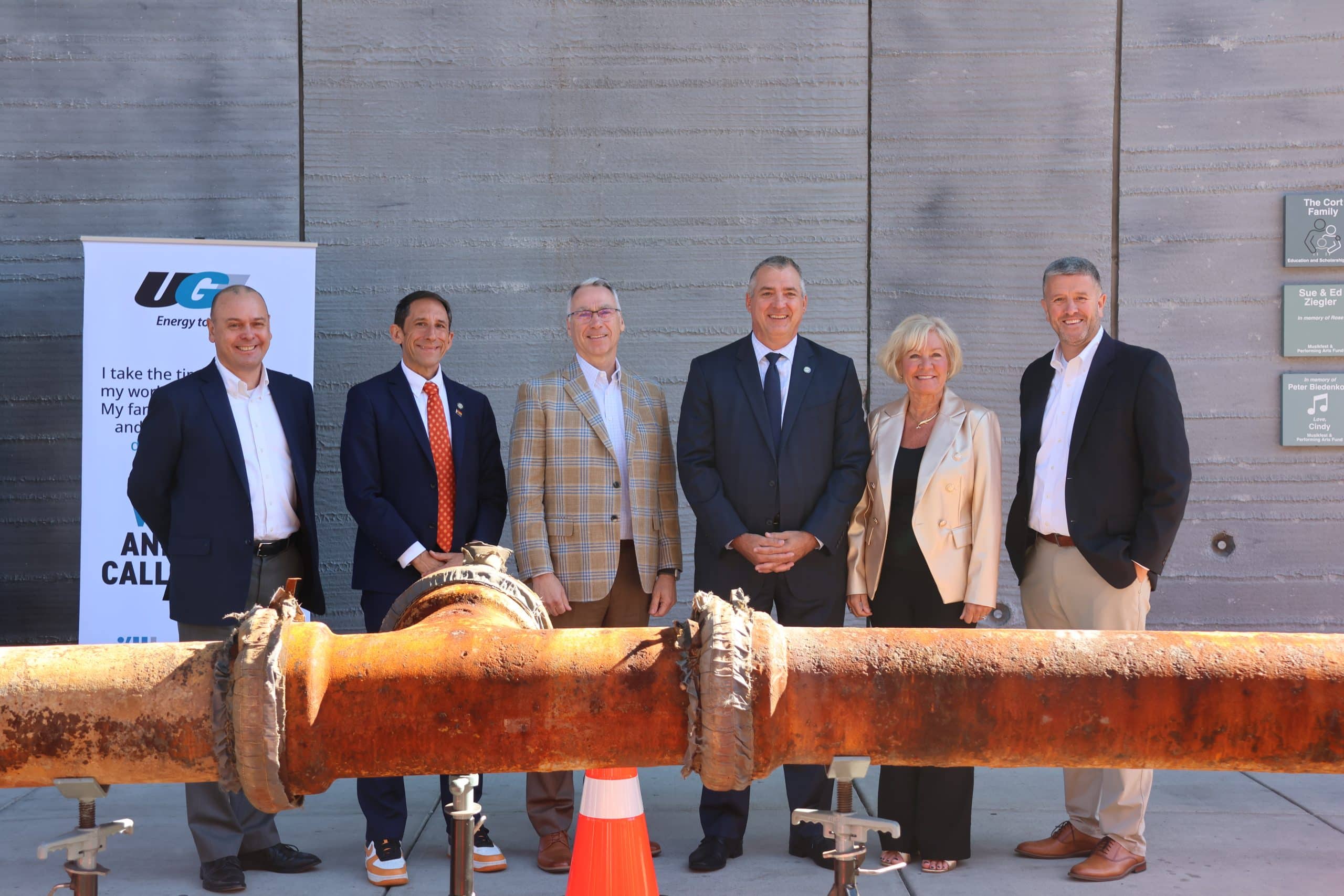 UGI leadership, legislators, and PUC officials stand with piece of cast iron pipe.