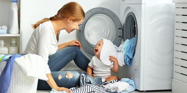 Baby and mother folding clothes by the dryer
