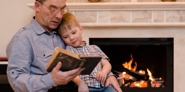 grandfather to his grandson reading a book by natural gas fireplace
