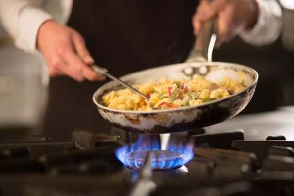 Cook preparing pasta dish over natural gas stoves